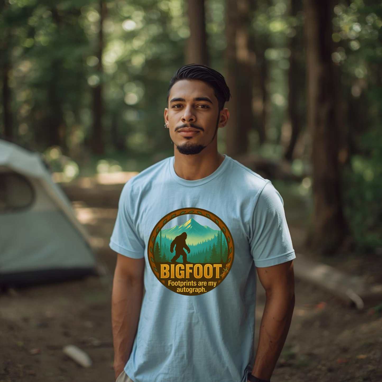 Man wearing a light blue t-shirt with a Bigfoot graphic in a forest setting