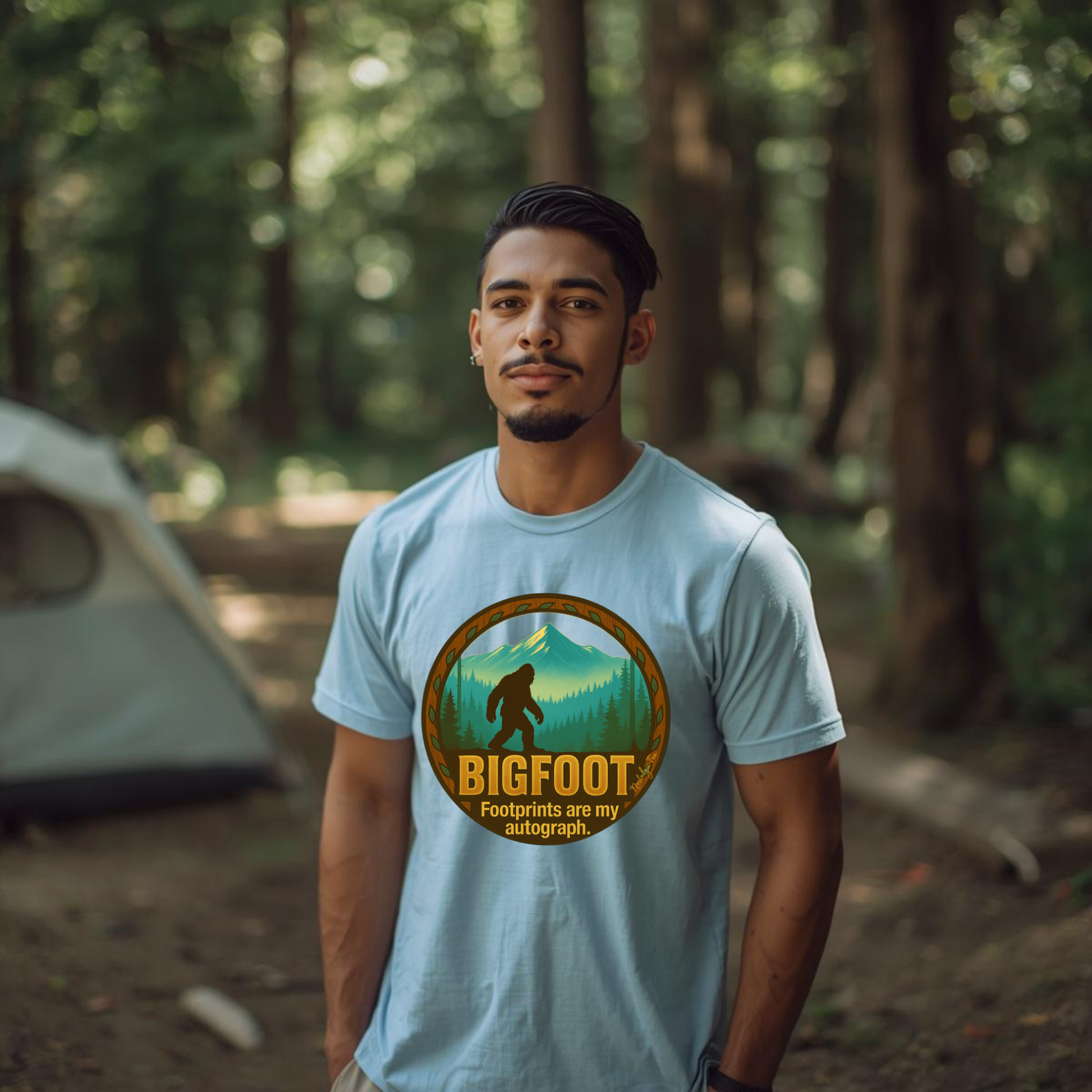 Man wearing a light blue t-shirt with a Bigfoot graphic in a forest setting