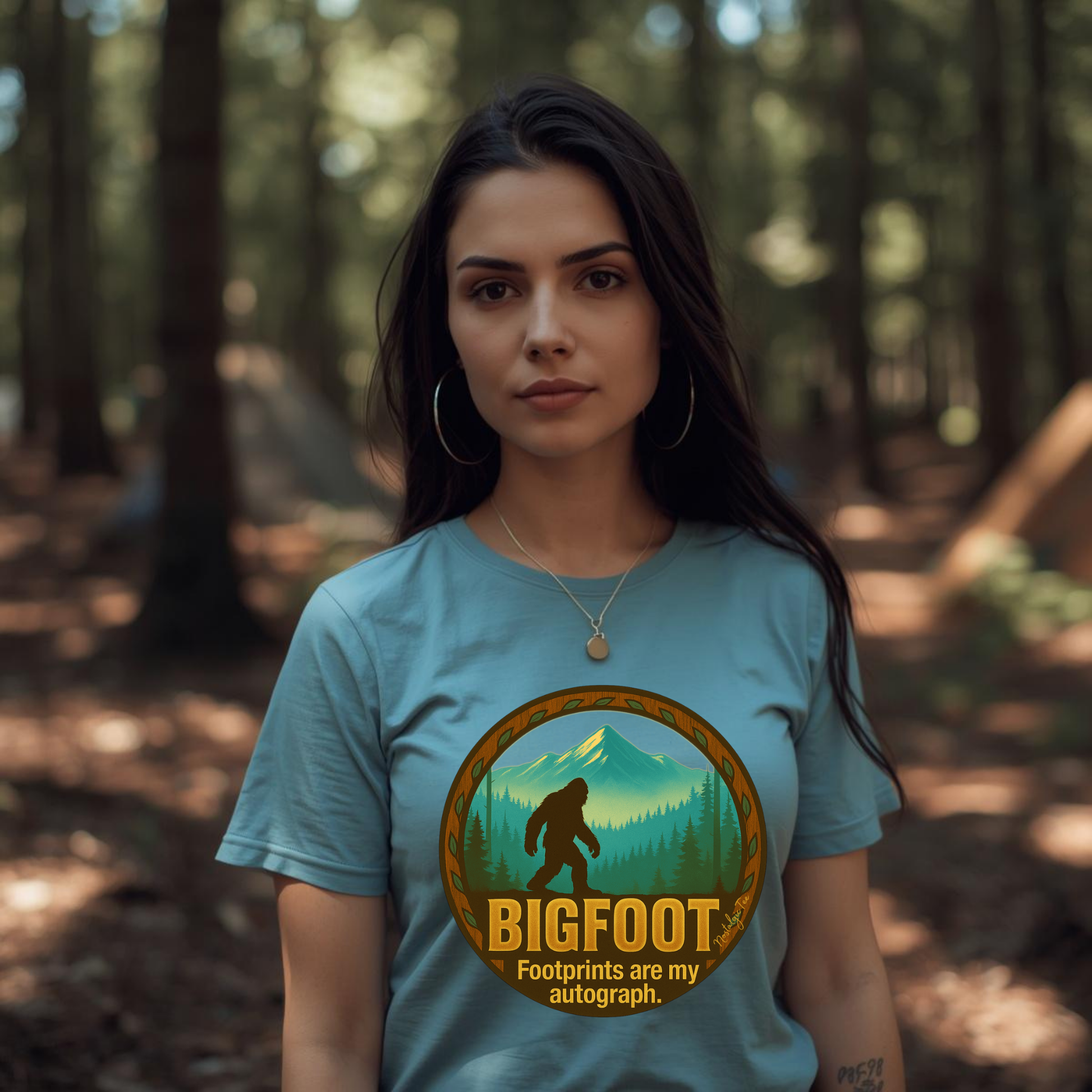 Woman wearing a blue t-shirt with a Bigfoot graphic and text in a forest setting