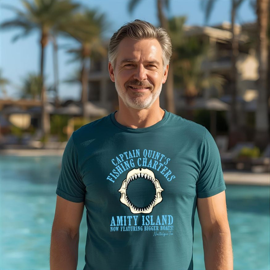 Man wearing a green t-shirt with a shark graphic and text, standing by a pool with palm trees in the background.